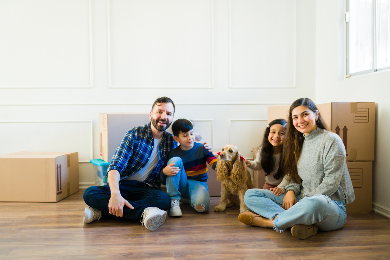 Happy family with little kids and dog happy about being home owners with a lot of boxes moving to a new house